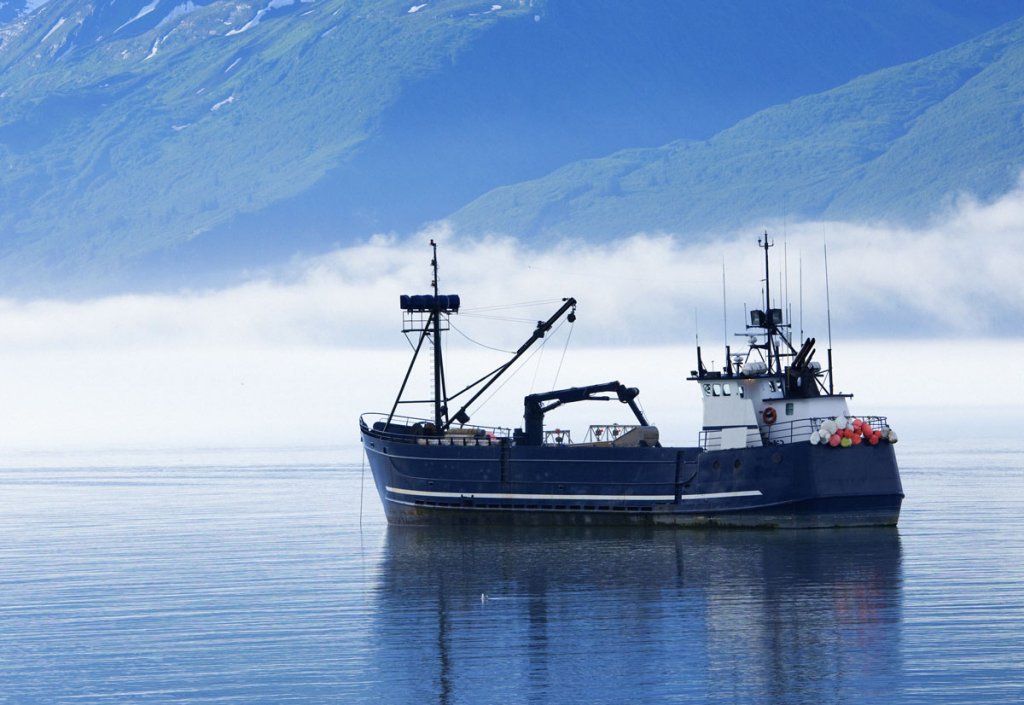 A deep blue fishing trawler at anchor on a calm misty sea
